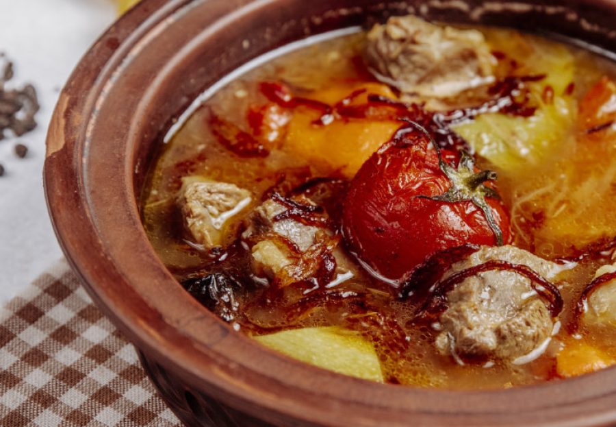side view of meat with potatoes and tomatoes in a clay pot